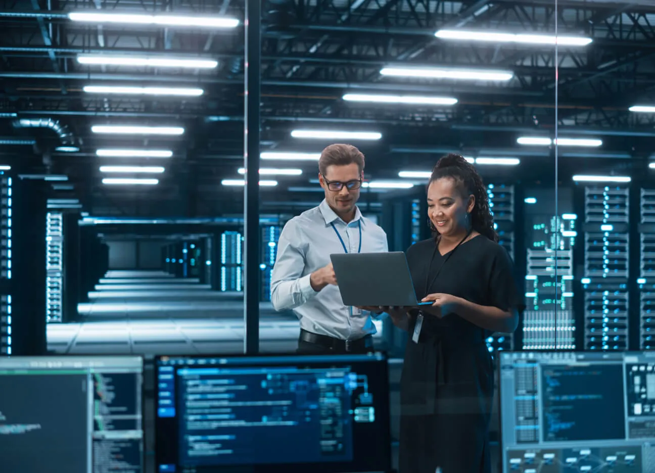 Two engineers in a data room looking at a laptop smiling