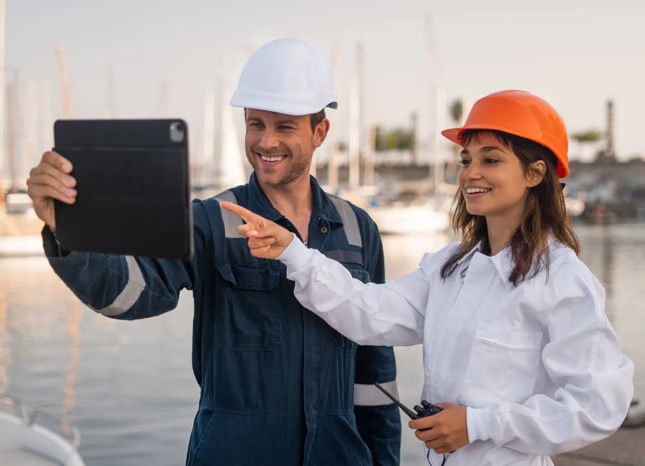 Two engineers, with safety helmets, looking at a tablet and smiling