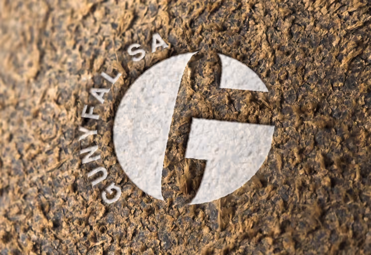 The logo of Gunyfal SA is displayed on a rough, brown textured background. The logo consists of a stylized capital letter "G" formed by negative space within a circular shape, with the text "GUNYFAL SA" curved around the left side.