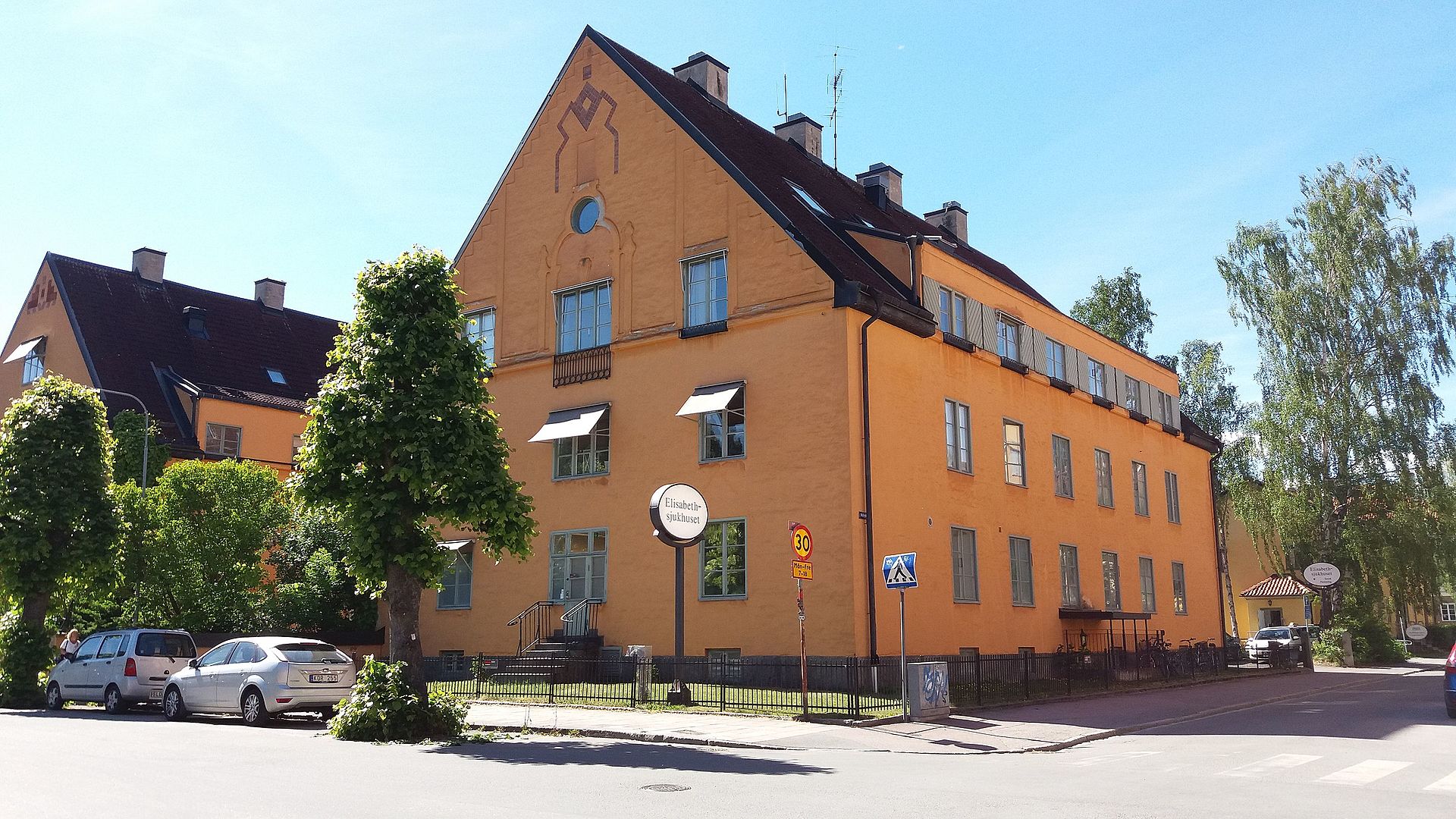 The warm yellow main building of Aleris Elisabethsjukhset photographed from the street on a bright Summer day.