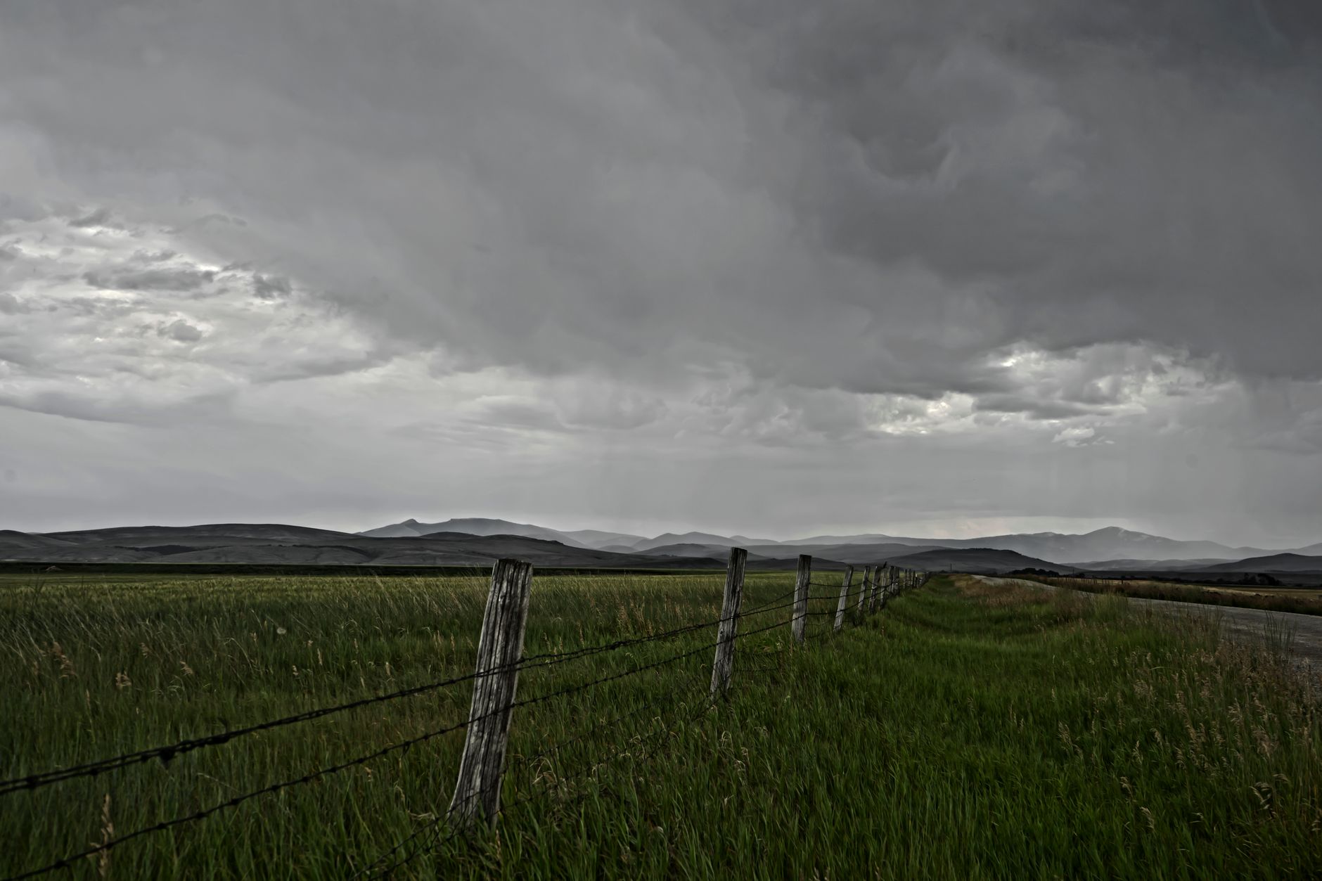 A moody, overcast day over a rural Montana landscape with barbed wire fence and mountains.