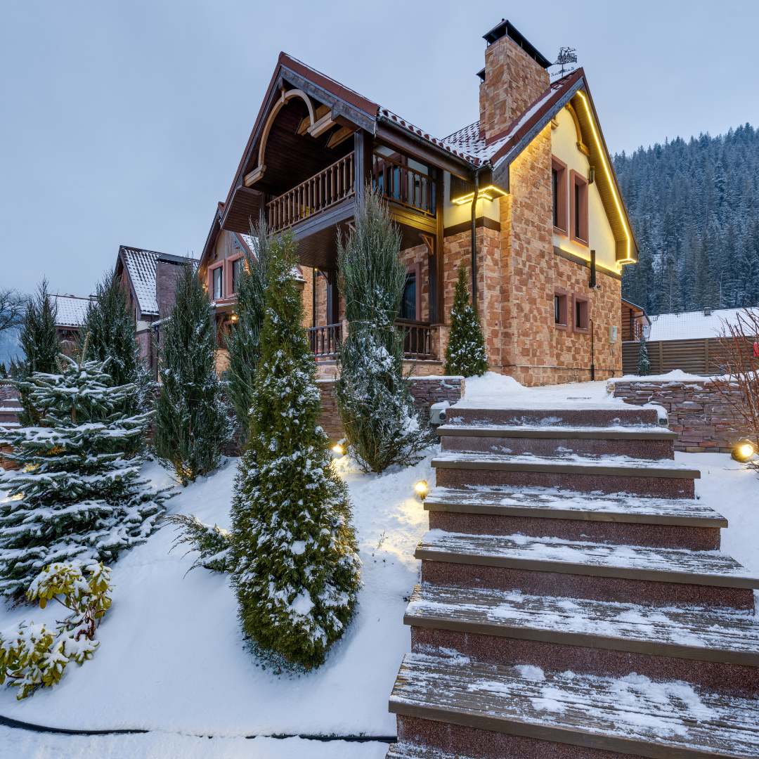 Snow-covered mountain home with evergreen landscaping and stone steps, highlighting winter-ready out