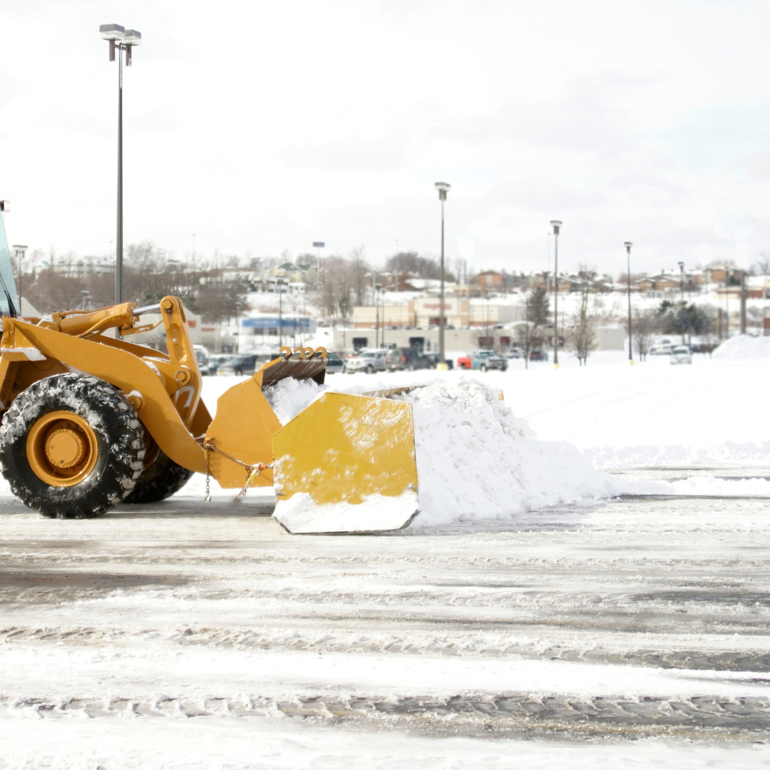 Heavy equipment plowing snow in a commercial parking lot, illustrating professional snow removal.