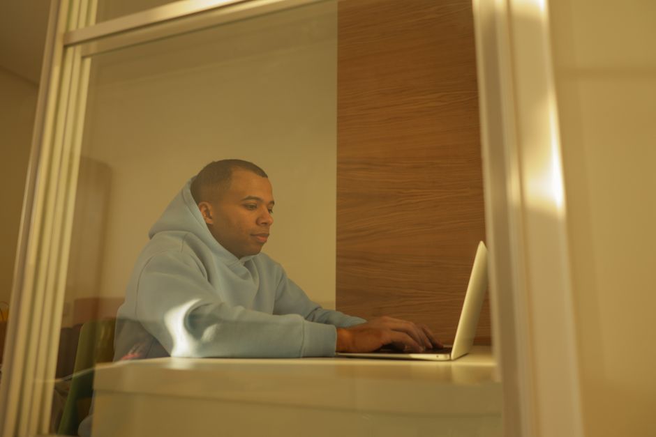 African American man working on a laptop indoors, viewed through glass.