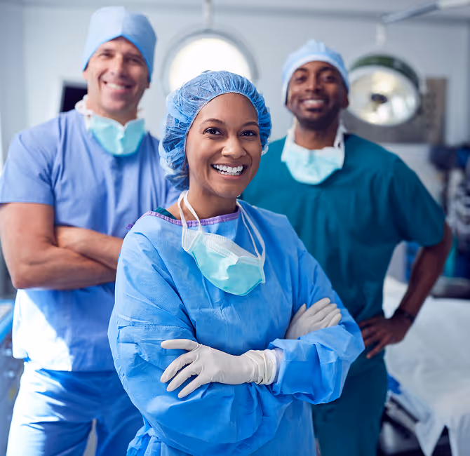 Three smiling healthcare professionals in surgical scrubs, caps, and masks standing confidently in a medical setting.