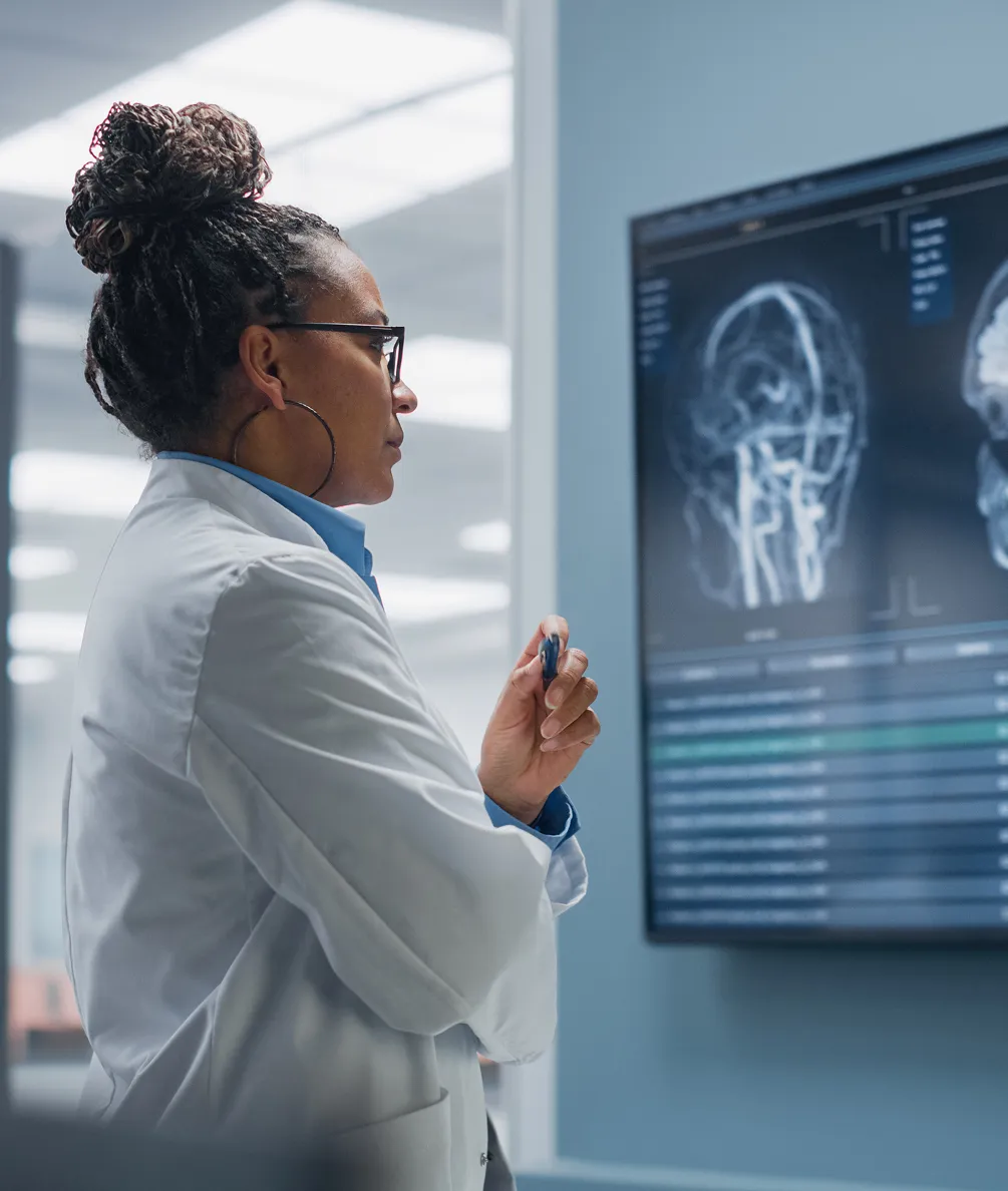 Female doctor with glasses and braided hair examining brain scans on a digital screen.