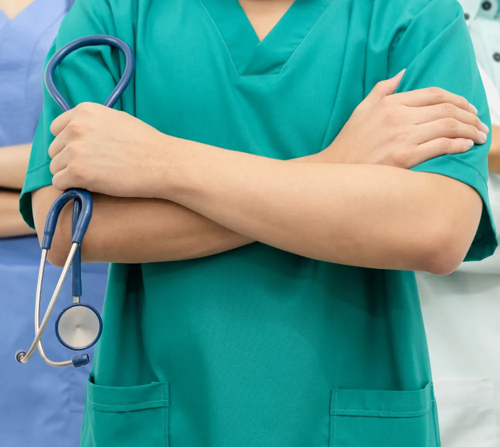 Medical professional in green scrubs holding a stethoscope with arms crossed.
