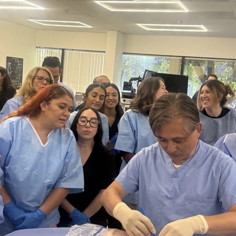 Medical team wearing scrubs and gloves attentively watches Dr. Yoo performing a procedure indoors.
