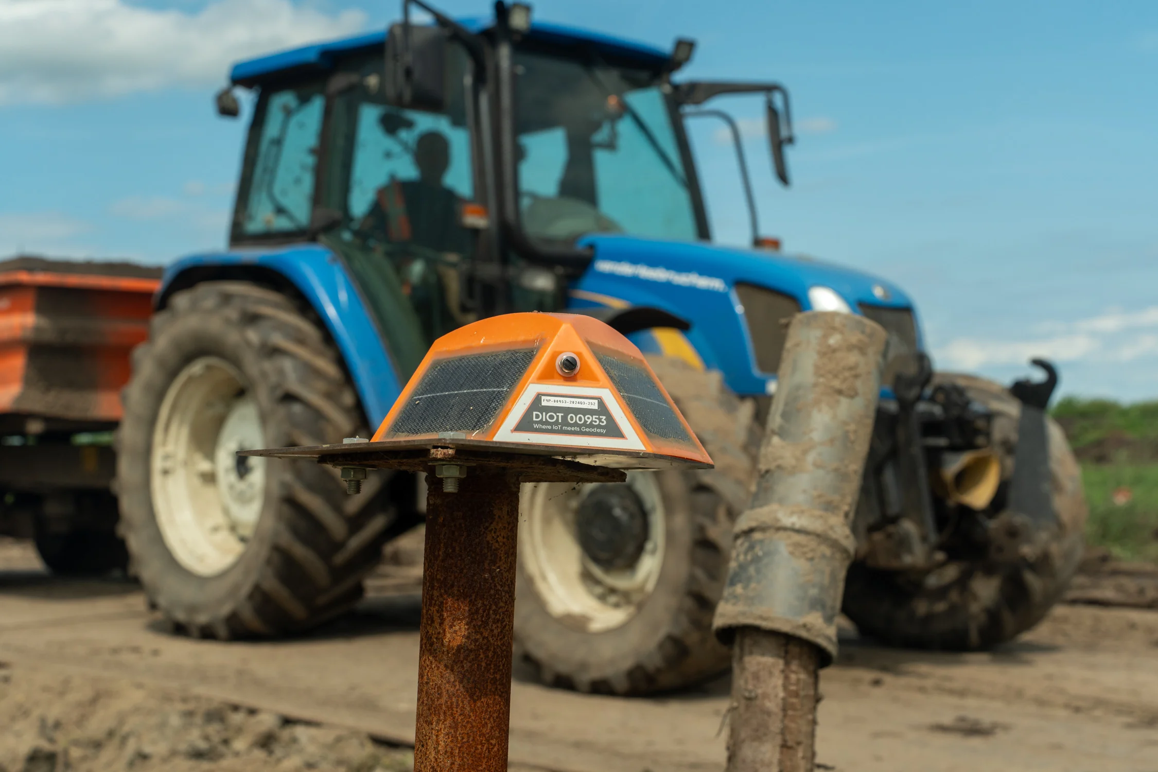 Zakbaken in de voorgrond geplaatst in de bodem, met een blauwe tractor van van der Lee Bruchem onscherp op de achtergrond tijdens werkzaamheden aan de kadeversterking in Giessenburg.