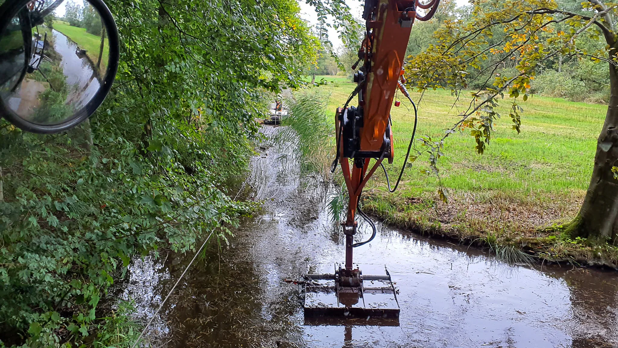 Kraan van Van der Lee voert baggerwerkzaamheden uit met een zuiger in een smalle watergang tussen bomen.