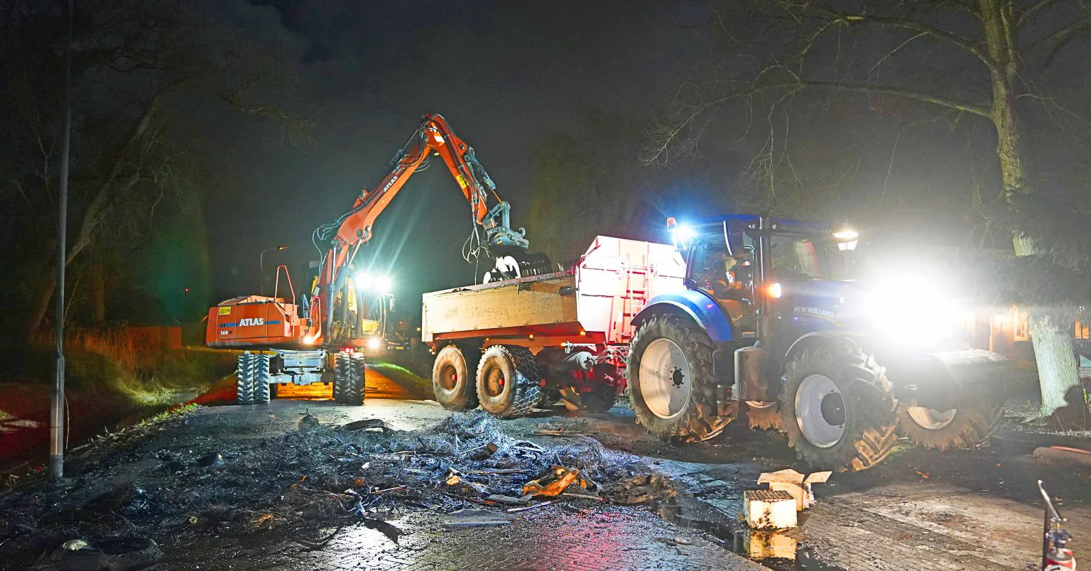 Atlas kraan en tractor met aanhanger van Van der Lee ruimen puin op van een afgebrande stapel