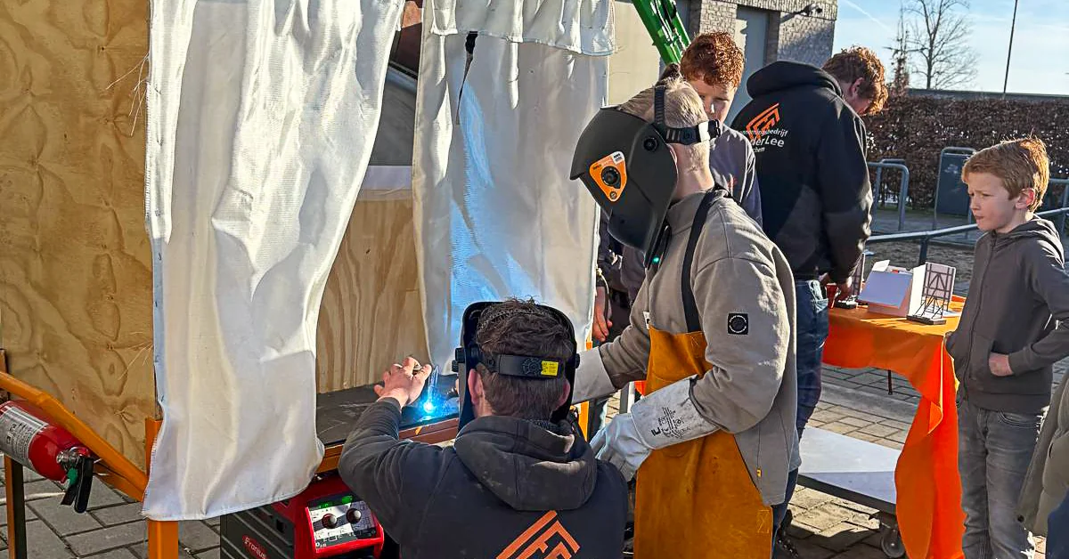 Een leerling last onder begeleiding van een VDL-medewerker in de lascabine buiten op het schoolplein van Gomarus