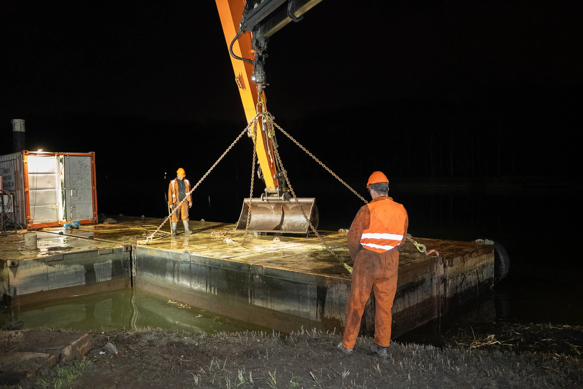 Twee medewerkers begeleiden het terugplaatsen van een ponton op het water in het donker