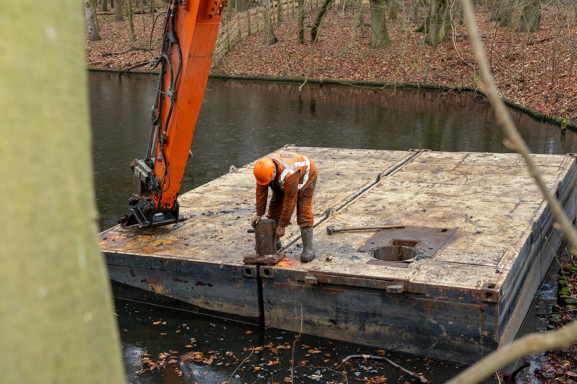 Medewerker van Van der Lee monteert onderdelen op een ponton in een bosrijke watergang