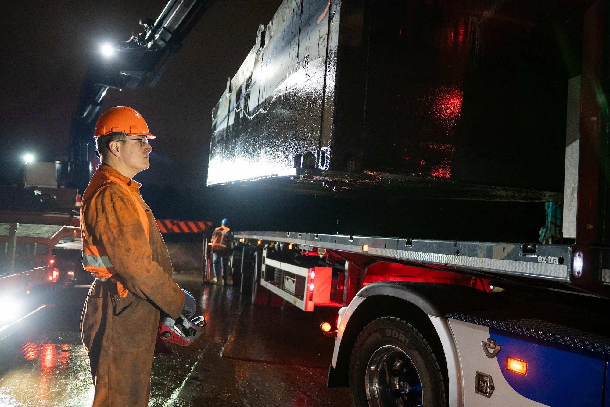 Chauffeur begeleidt het laden van een pontondeel op een vrachtwagen bij nachtelijke klus