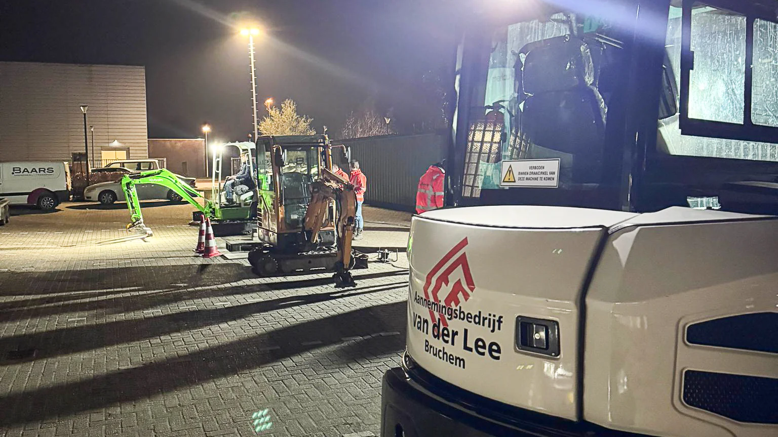 Meerdere mini graafmachines van Van der Lee Bruchem staan opgesteld op een verlicht terrein tijdens een avondtraining of demonstratie