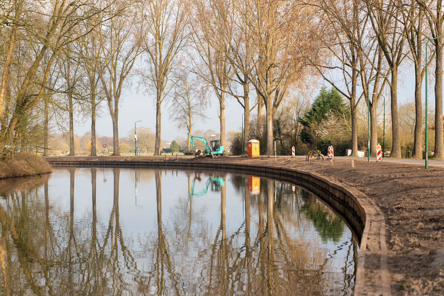 Overzicht van werkzaamheden langs een watergang met graafmachine en nieuwe oeverconstructie langs een bocht