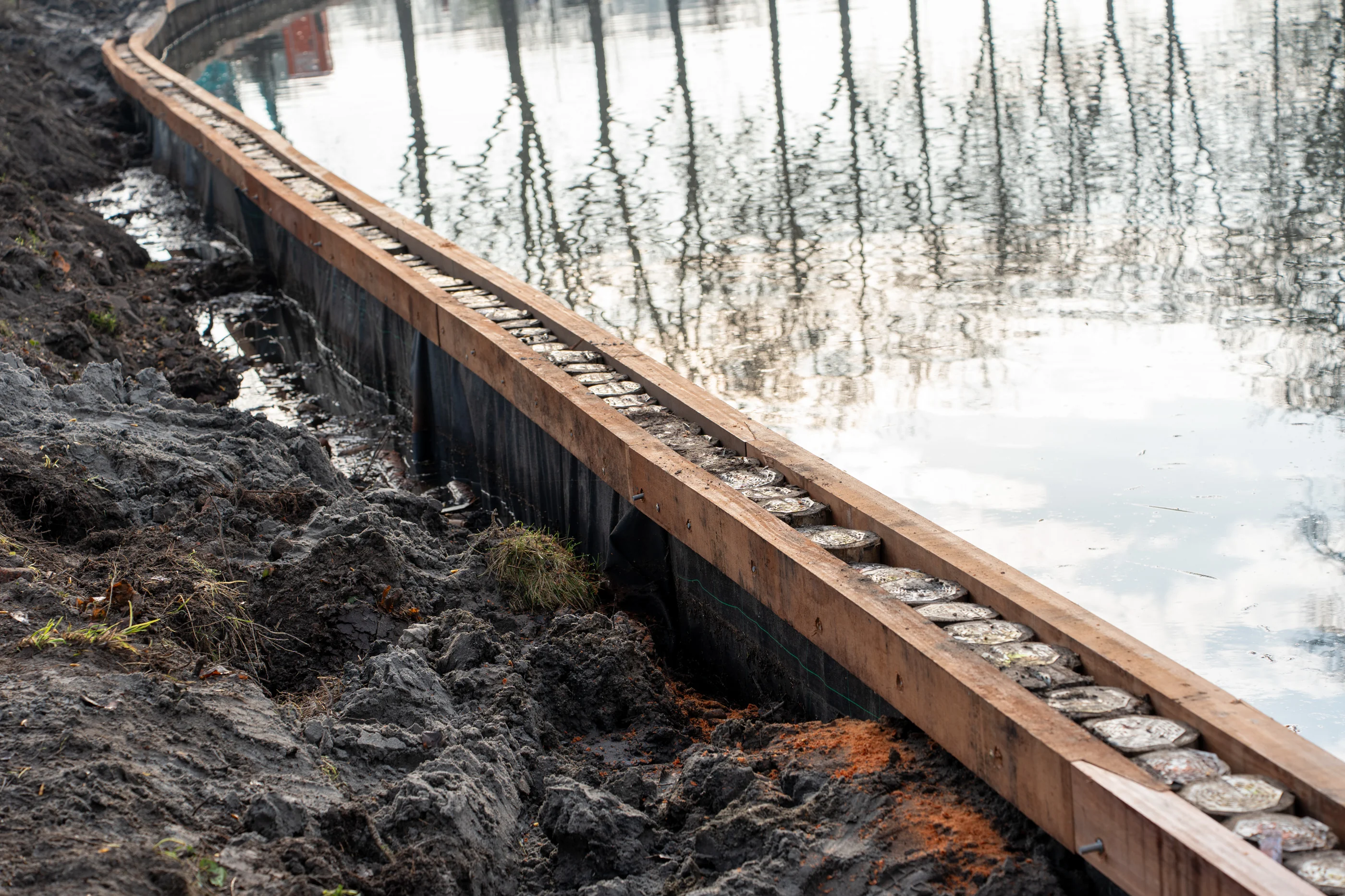 Detail van houten beschoeiing langs het water tijdens aanleg van een nieuwe oeverconstructie