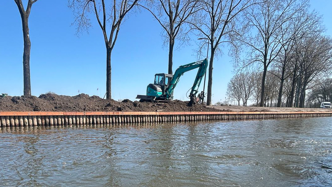 Nieuwe palenrij beschoeiing langs de Vecht in Stichtse Vecht, met rupskraan aan het werk op de oever en recent aangebrachte gording zichtbaar langs de waterlijn.