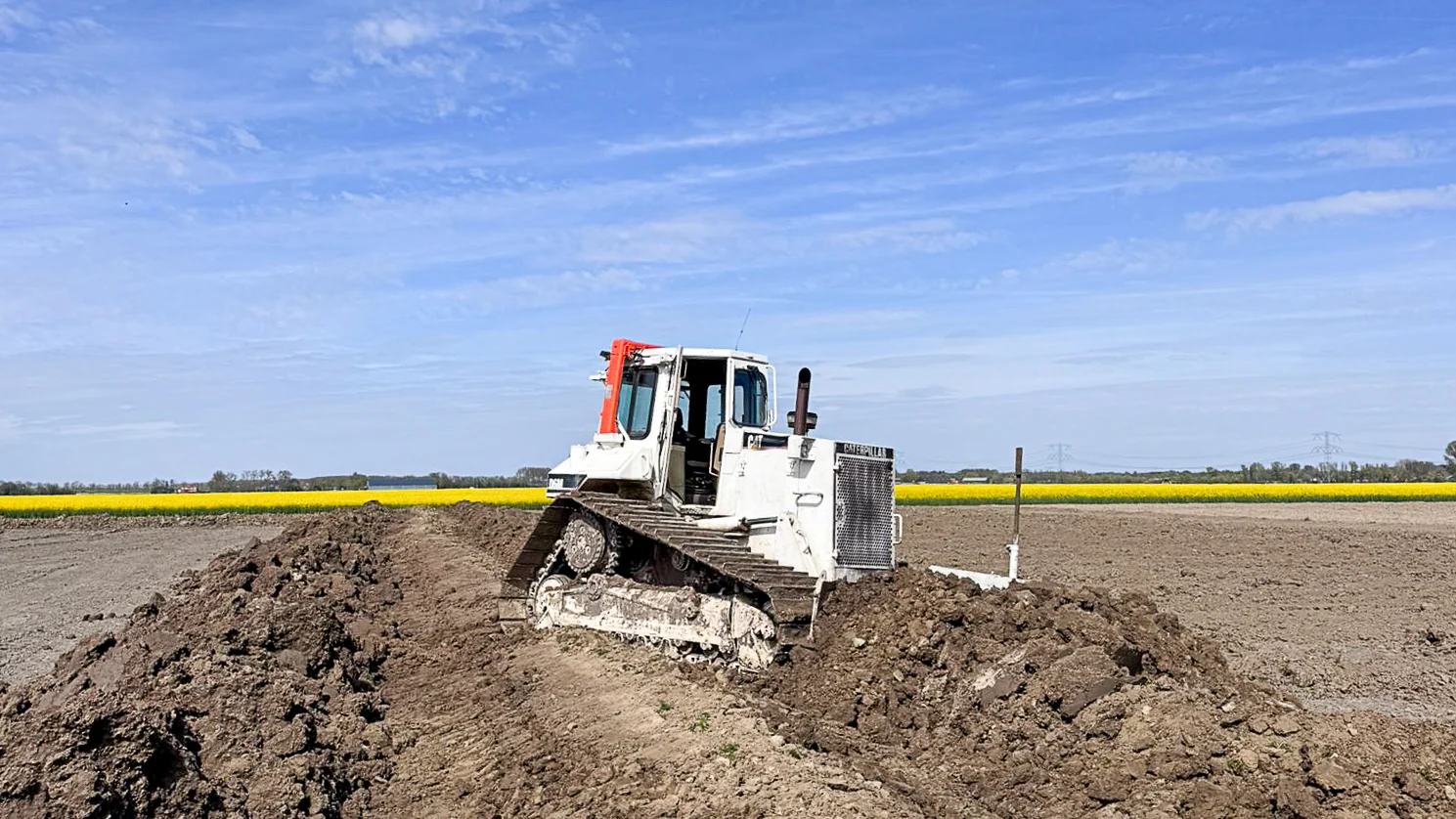 Caterpillar bulldozer voert grondverzetwerkzaamheden uit op een landbouwperceel tijdens het egaliseren van terrein in Halsteren.