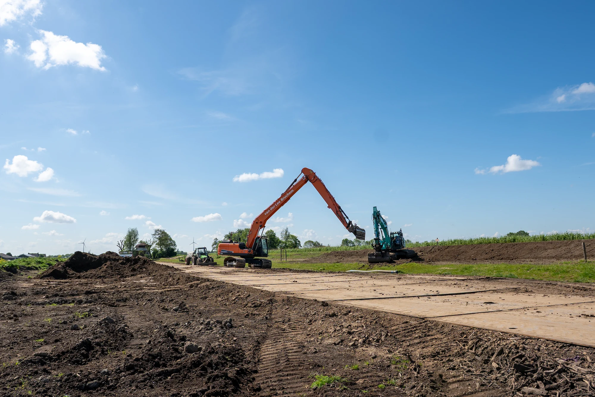 Overzichtsfoto van grondverzetwerkzaamheden met graafmachines, bouwweg en watergang in het buitengebied.