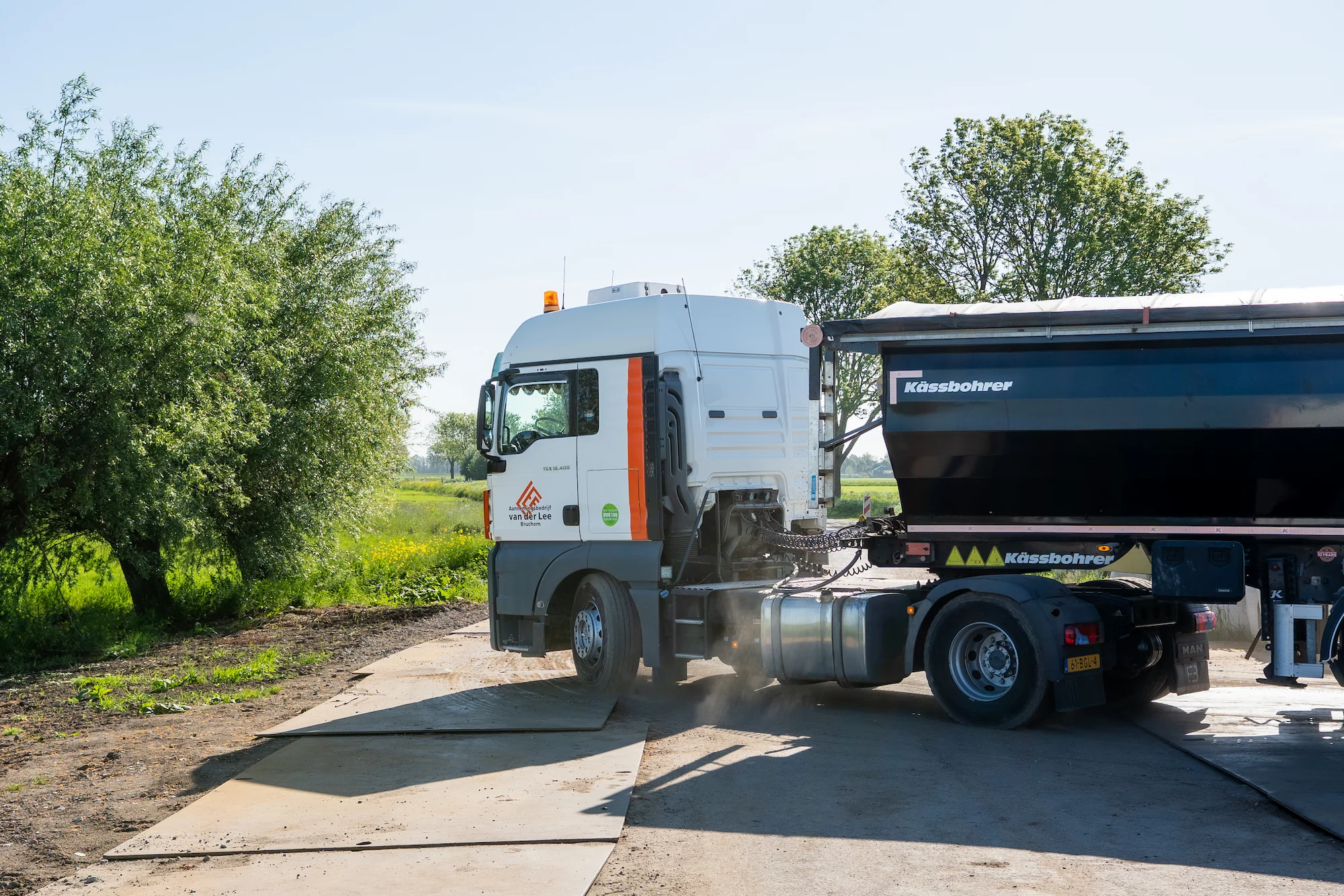 Vrachtwagen met oplegger rijdt over rijplaten tijdens werkzaamheden aan een watergang door Van der Lee Bruchem.