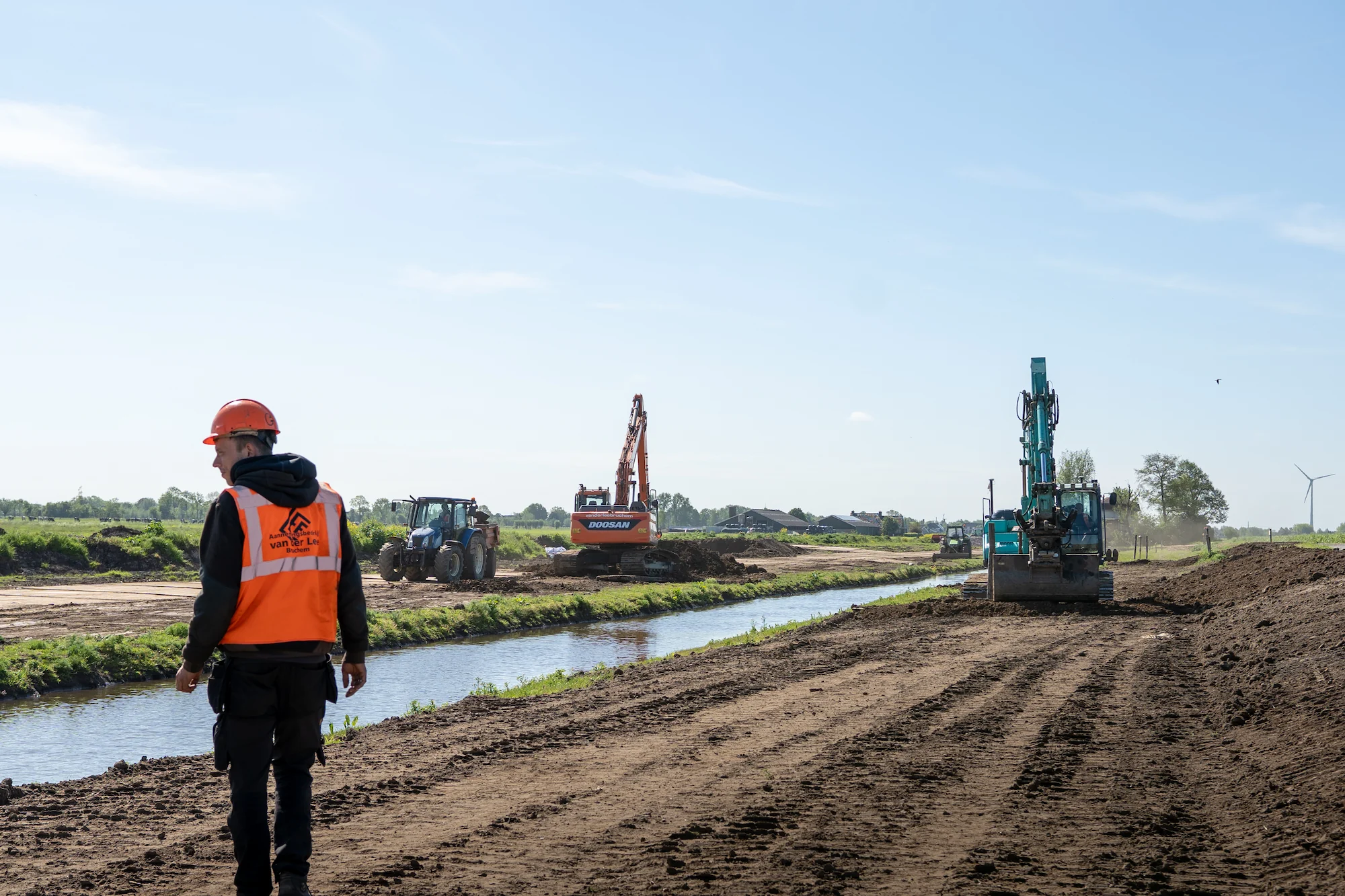 Medewerker van Van der Lee Bruchem houdt toezicht op grondwerkzaamheden langs een watergang in landelijk gebied.