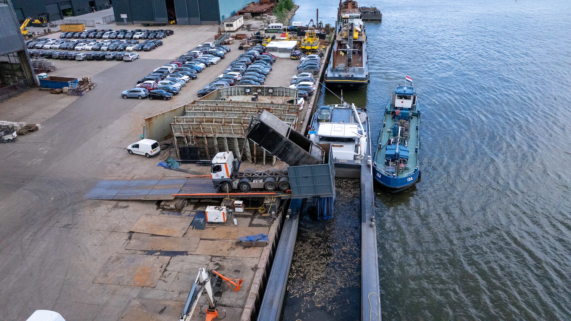 Vrachtwagen stort bagger over in een binnenvaartschip voor verdere afvoer vanaf de overslaglocatie.