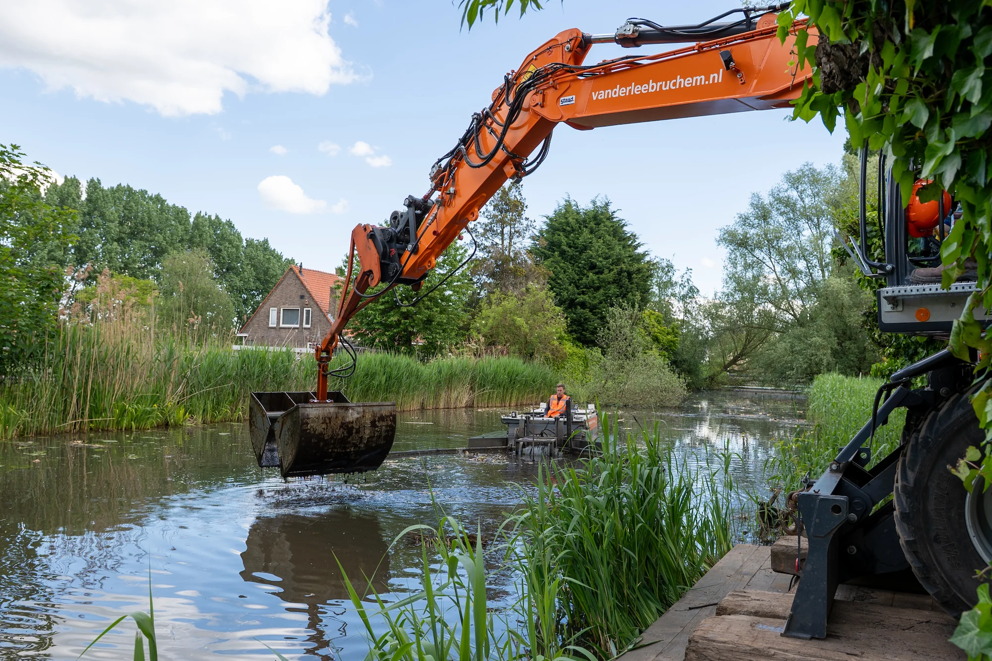 Elektrische mobiele kraan werkt samen met een elektrische schuifboot tijdens emissieloze baggerwerkzaamheden in een stedelijke watergang.
