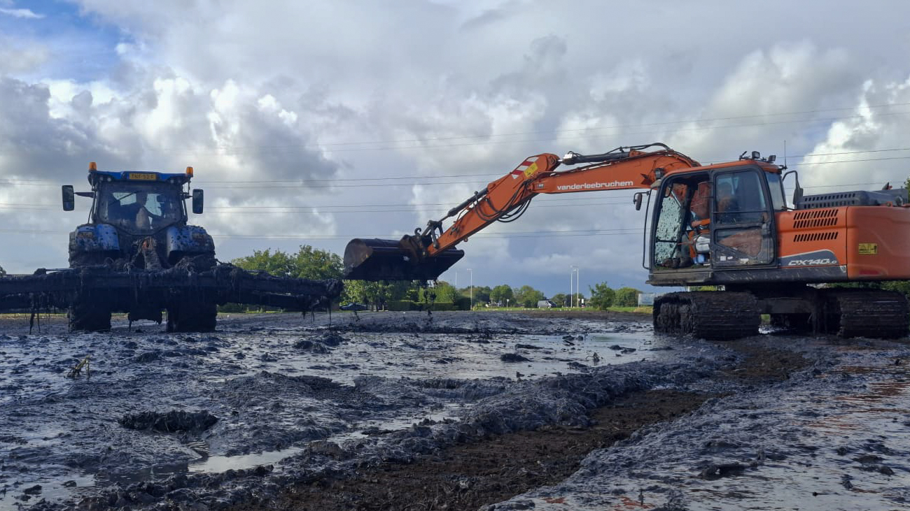 Tractor en rupskraan van Van der Lee Bruchem in de modder tijdens baggerwerkzaamheden.