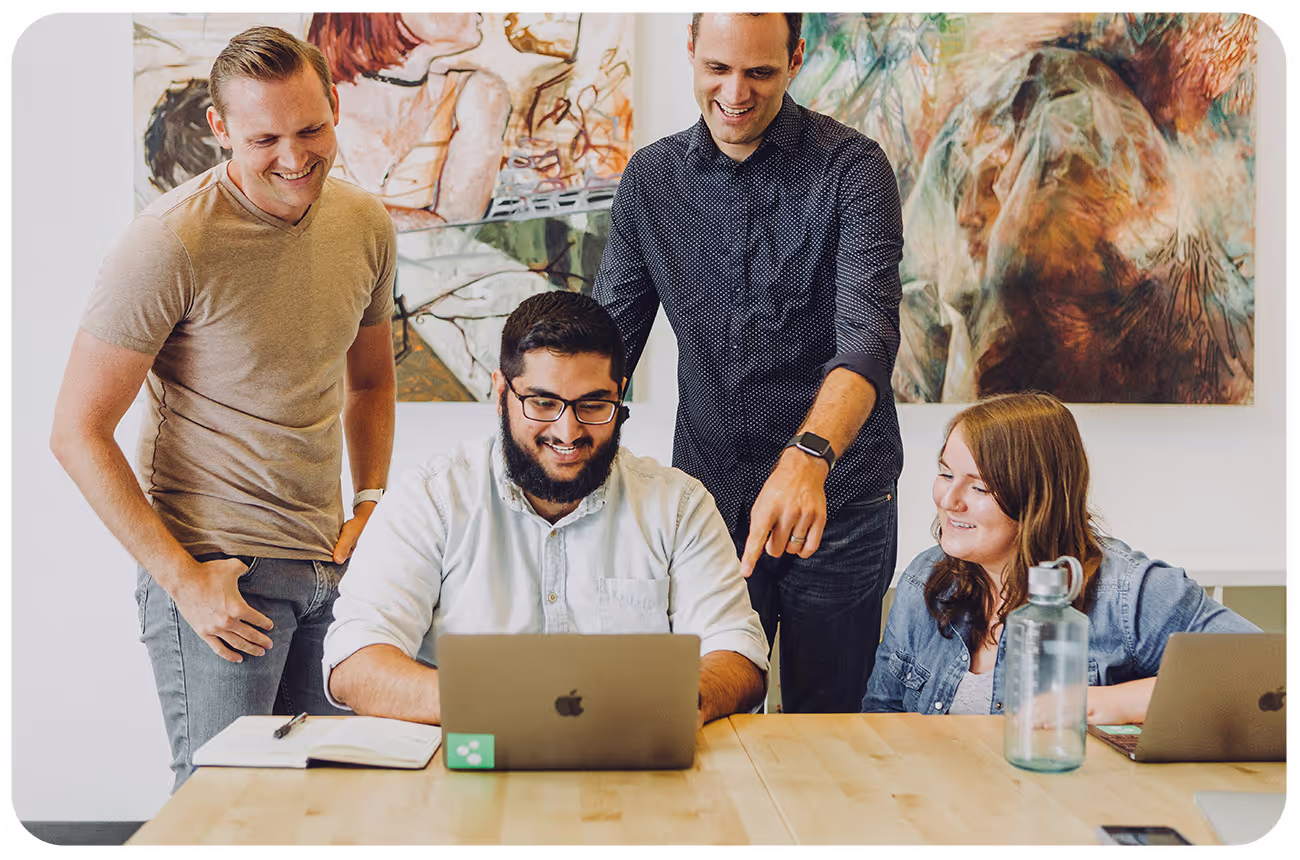 Group of people gathered around a laptop computer and smiling