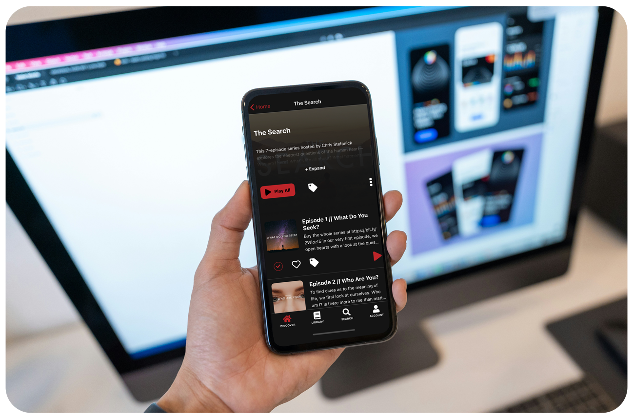 Someone holding phone with an app built by Annunciate featuring a video series with a computer in the background