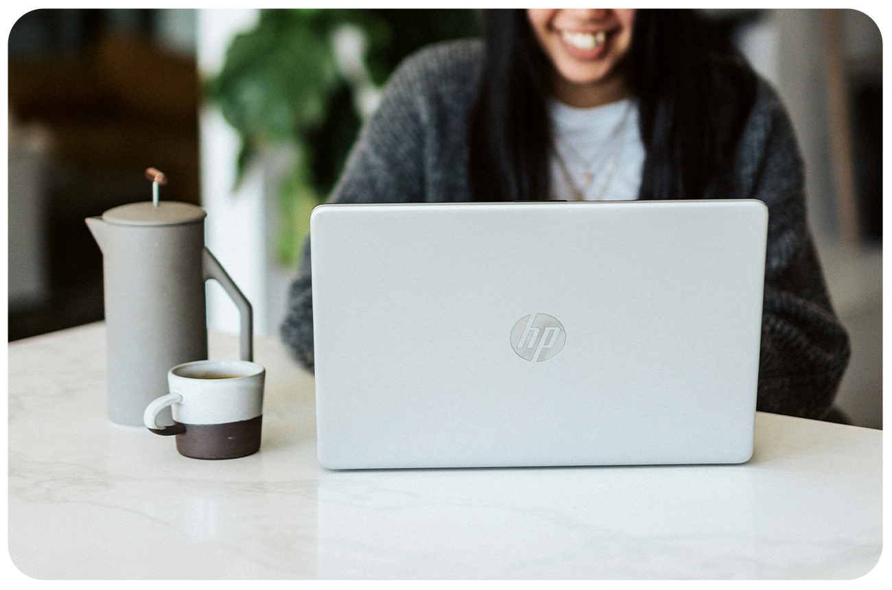 Woman sitting at a laptop with a French press and coffee mug