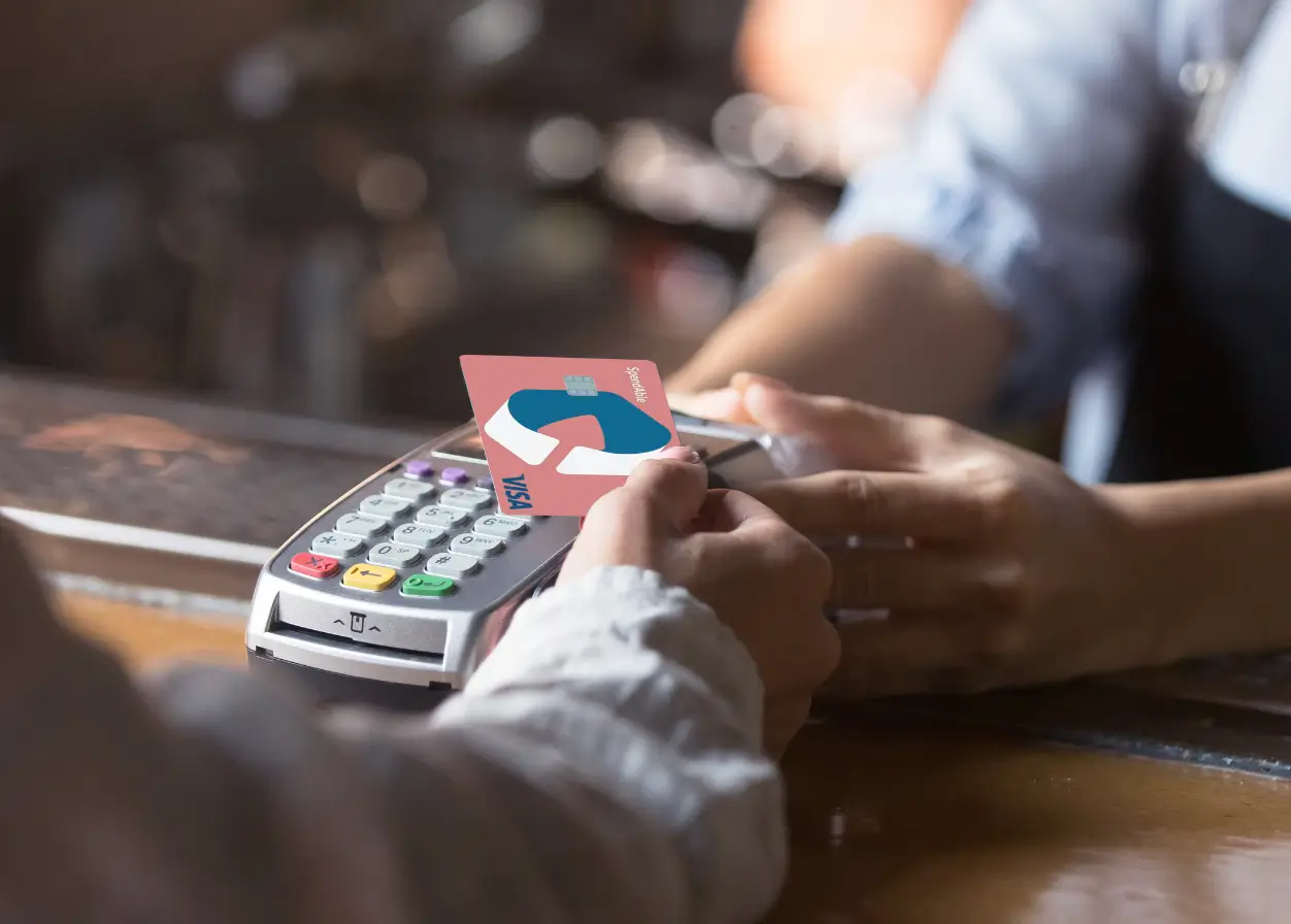 Close-up of a person paying at a card machine with a SpendAble Visa, showing how a debit card for daily expenses makes shopping simple.