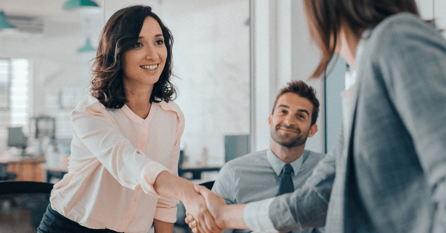A woman in business professional reaching to shake another womans hand.