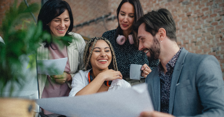 A woman smiling, surrounded by people in business casual holding papers.