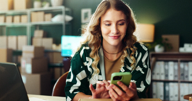 a woman seated looking at her phone with a smile.