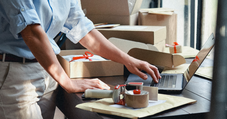 A man works on a laptop, surrounded by packing supplies.