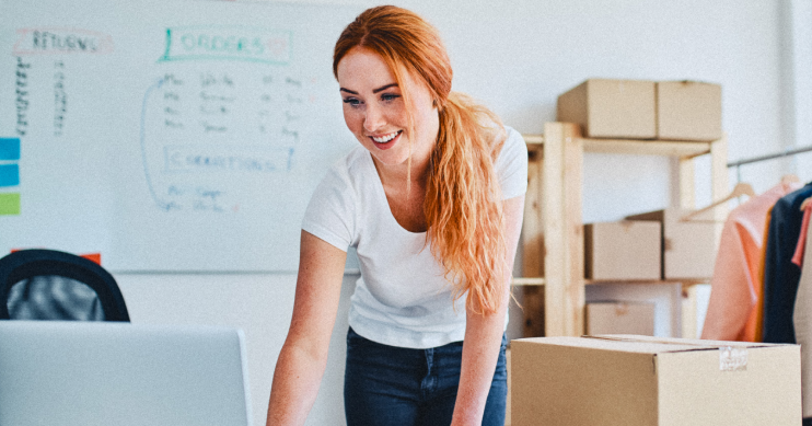 A woman leans over her desk to look at her laptop.