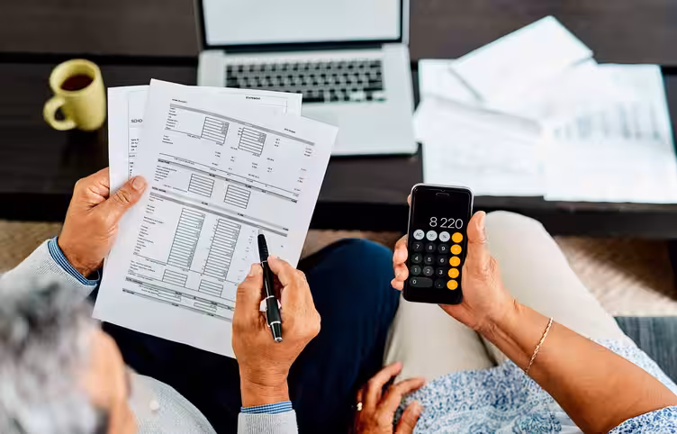 A couple reviews financial statements, balance sheets, and income statements, using a calculator for small business financial planning.