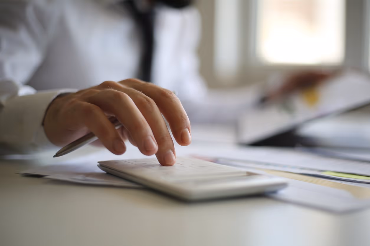 A person's hands operating a calculator with a sheet of paper underneath, illustrating the calculation for the units of production depreciation method.
