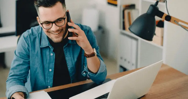 Man on cell phone in front of a laptop