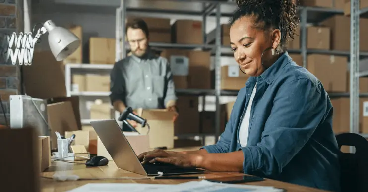 A woman sits at a desk in a warehouse on her laptop.