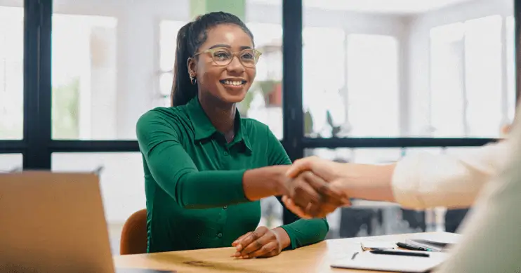 a woman in a green blouse shakes hands across a desk
