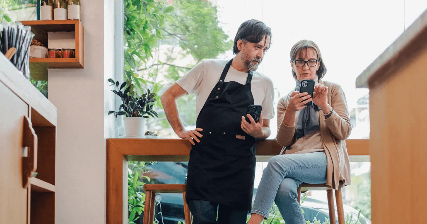 a seated woman showing her iPhone phone screen to a man in an apron.