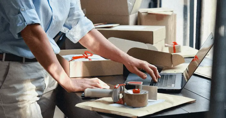 A man works on a laptop, surrounded by packing supplies.
