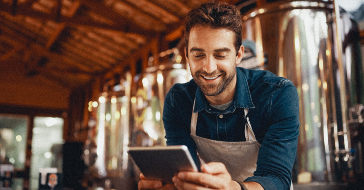 A man leans over acounter and smiles at his phone.