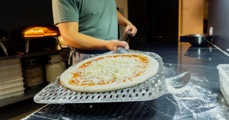a man slides a pizza into an oven on a spatula