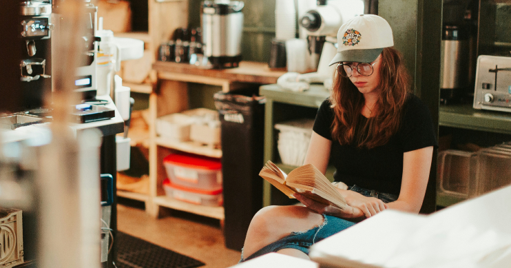 A cafe employee reads a book behind a counter.