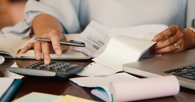 a woman uses a calculator with multiple papers and notepads in front of her.